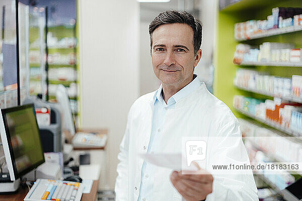 Smiling mature pharmacist showing prescription at store