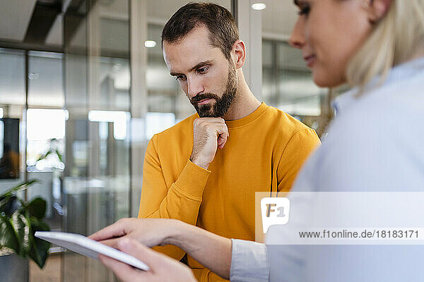 Dedicated businessman with hand on chin looking at tablet PC held by colleague