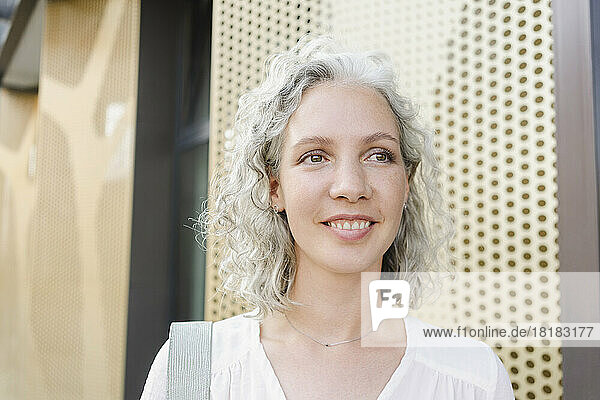 Smiling businesswoman with gray curly hair by wall