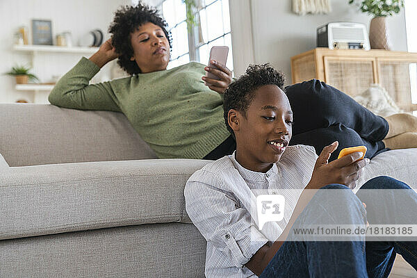 Smiling boy using smart phone with mother in background at home