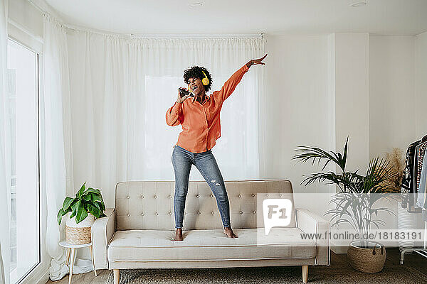 Carefree freelancer dancing and singing on sofa at home office