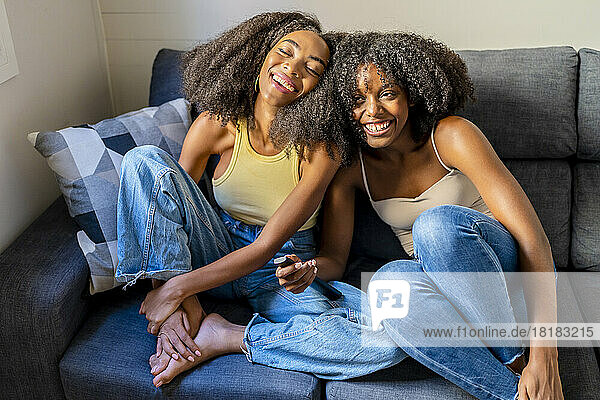 Young woman with remote control laughing by girlfriend in living room