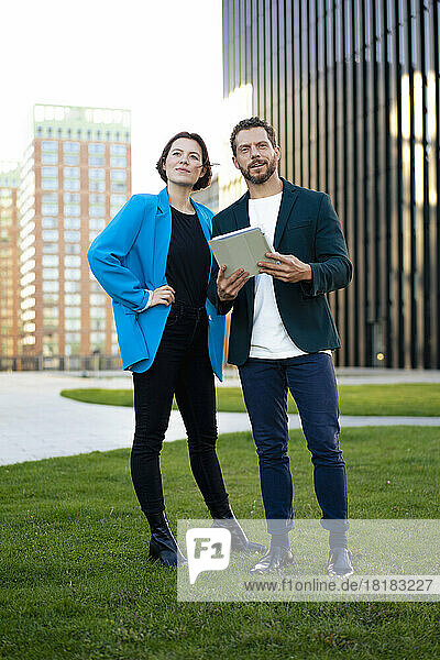 Businessman holding tablet PC standing with colleague on grass
