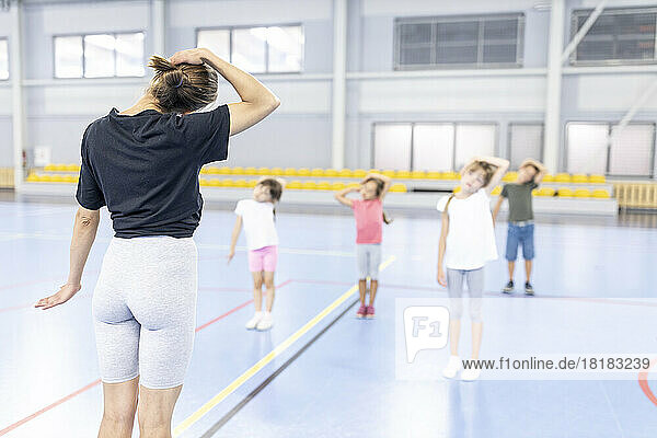 Teacher instructing students doing stretching exercises standing at school sports court