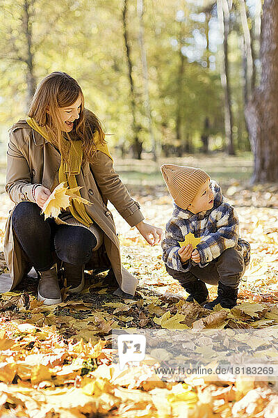 Happy mother and son in squatting position holding yellow leaf at park