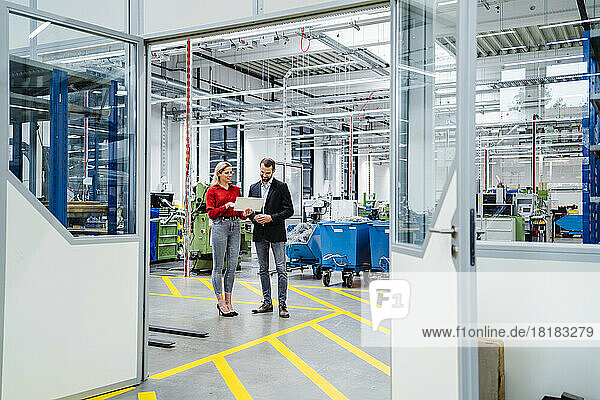 Businessman discussing with colleague holding tablet PC at factory seen through doorway