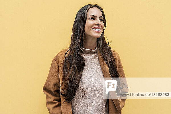 Smiling young woman in front of yellow wall