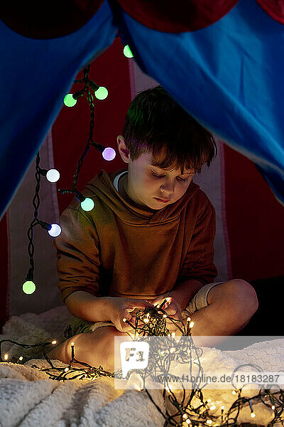 Boy playing with illuminated fairy lights in tent