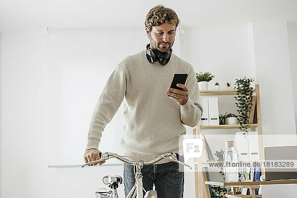 Businessman with bicycle using mobile phone in office