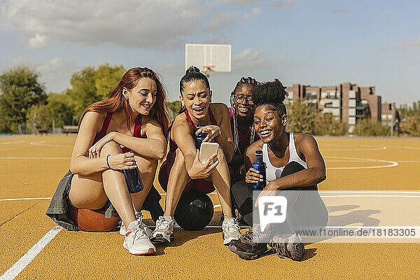 Happy young woman sharing smart phone with friends at sports court