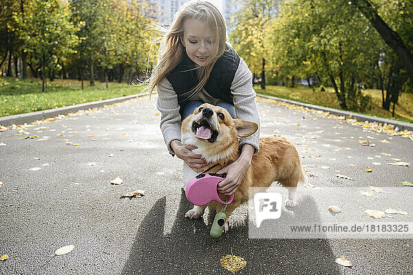 Woman adjusting pet leash of dog on road in autumn park