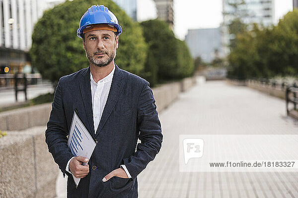 Contemplative engineer wearing hardhat standing at footpath