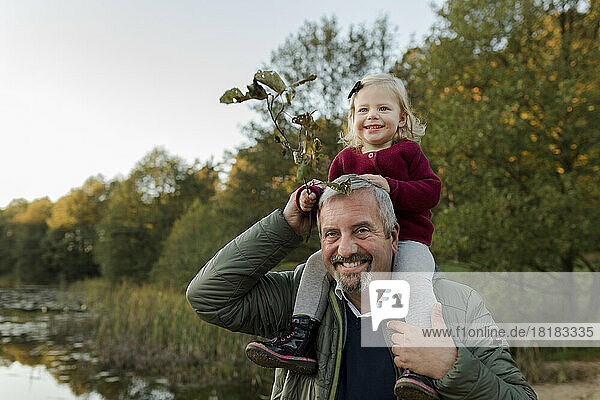 Lächelnder Mann mit Enkelin  die auf der Schulter sitzt und Pflanze hält