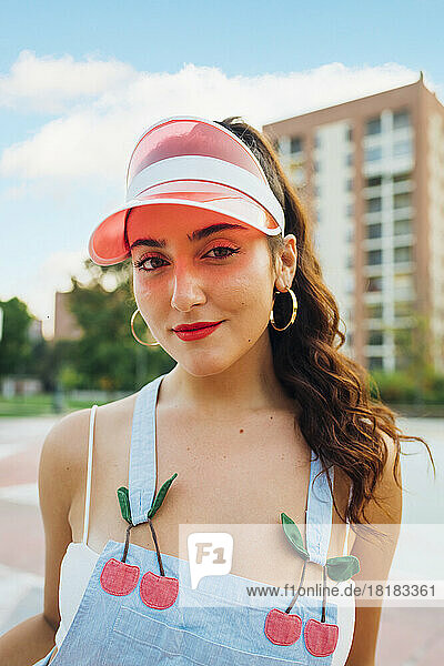 Smiling beautiful woman wearing sun visor standing at sports court