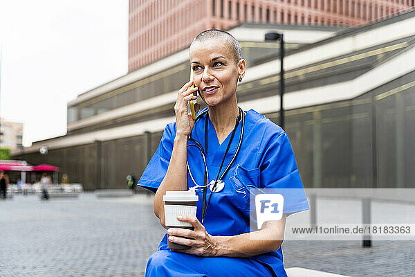 Smiling nurse with disposable coffee cup talking on mobile phone