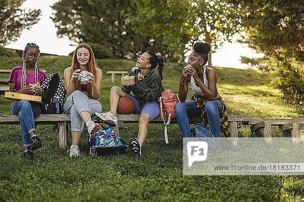 Fröhliche Freunde sitzen auf einer Bank und genießen das Essen im Park