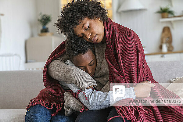 Mother embracing son wrapped in blanket at home