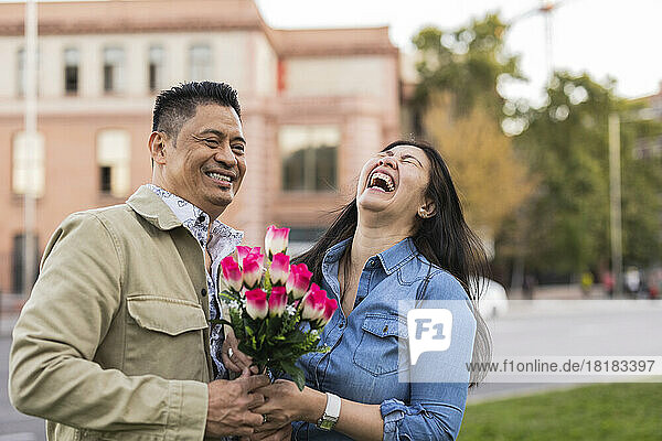 Happy mature couple holding flowers in front of building on Valentine's day