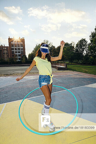 Smiling woman wearing roller skates practicing with hoop at sports court