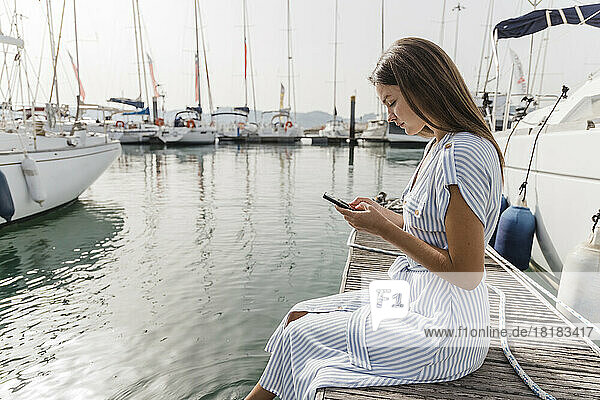 Young woman using smart phone sitting on jetty