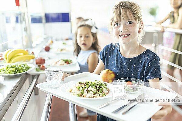 Smiling girl holding tray at lunch break in school cafeteria