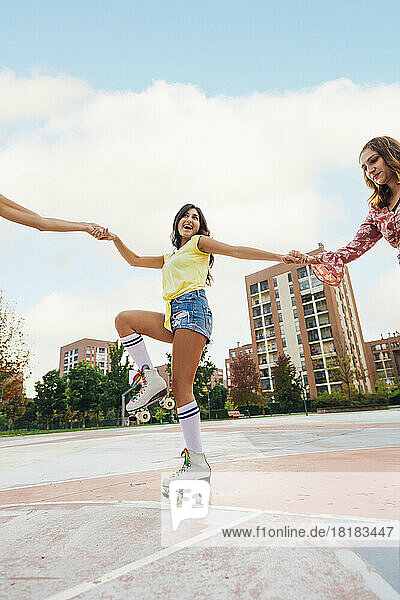 Smiling woman holding hands of friends roller skating at sports court
