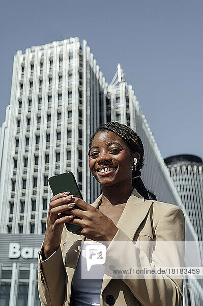 Happy young businesswoman with mobile phone outside building