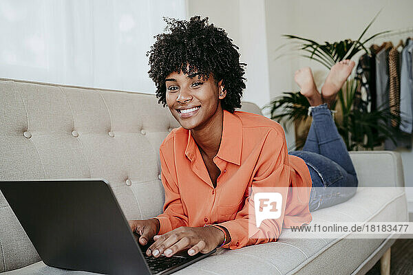 Happy freelancer with laptop lying on sofa at home office