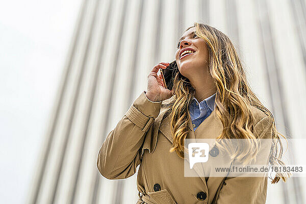 Glückliche Geschäftsfrau  die vor dem Gebäude mit dem Handy telefoniert