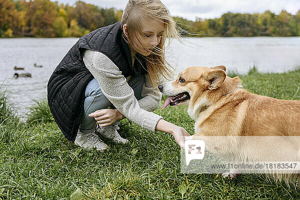 Woman doing handshake with dog on grass at lakeshore