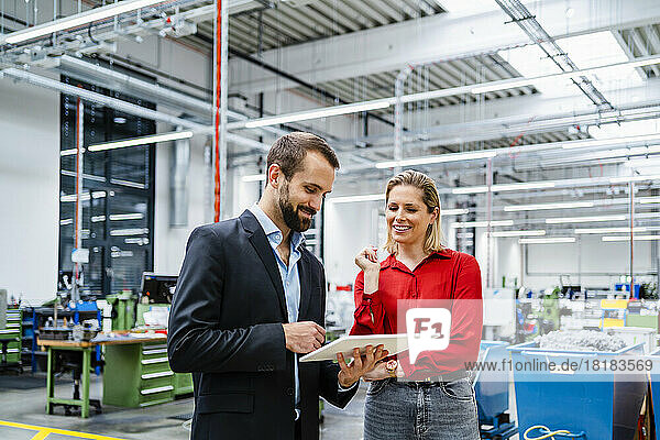 Smiling business colleagues with tablet PC standing in production hall