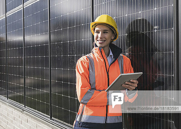 Happy female engineer with tablet PC leaning on solar panels