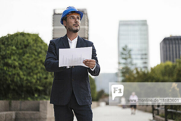 Businessman with hardhat holding chart on footpath