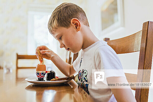 Großbritannien  trauriger Junge sitzt am Frühstückstisch und isst gekochtes Ei