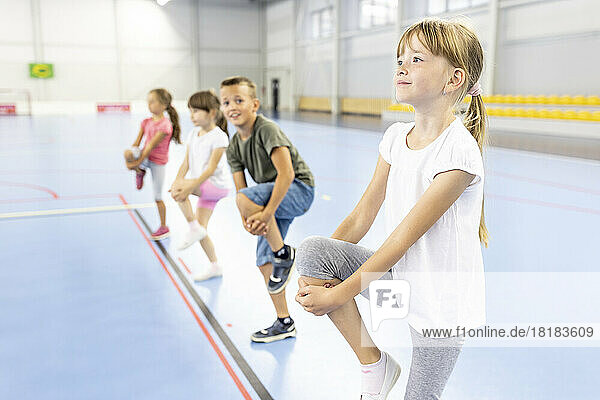 Girl stretching leg with students at school sports court