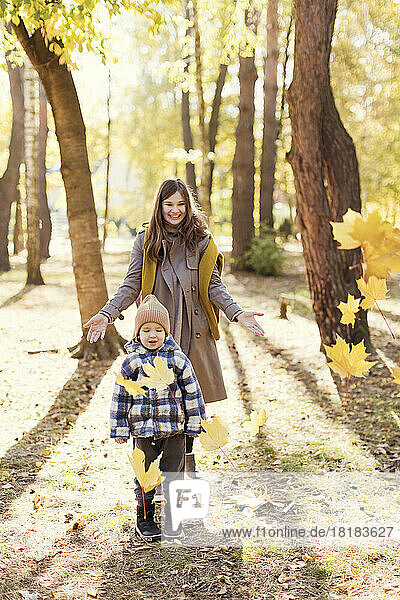 Mother throwing autumn leaves over son in park