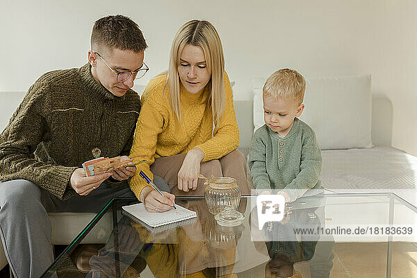 Young man and woman with son counting currency on table at home
