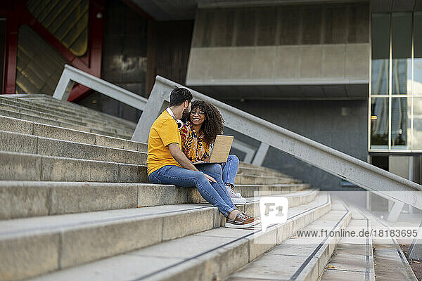 Happy young couple sitting with laptop on staircase