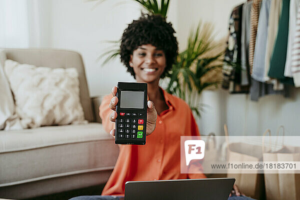 Happy businesswoman showing credit card reader at home office