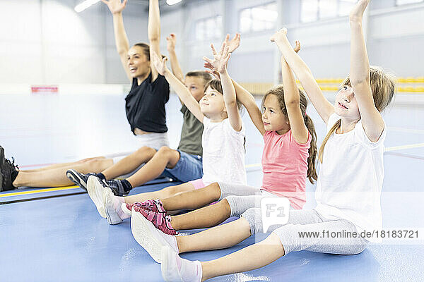Students doing exercise sitting with arms raised by teacher at school sports court