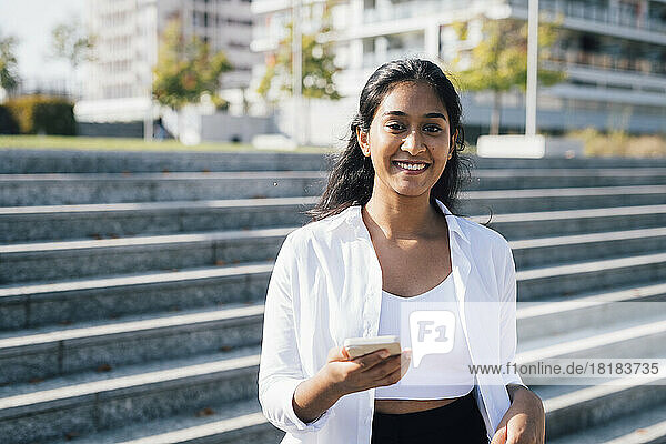 Smiling young woman with smart phone in front of steps