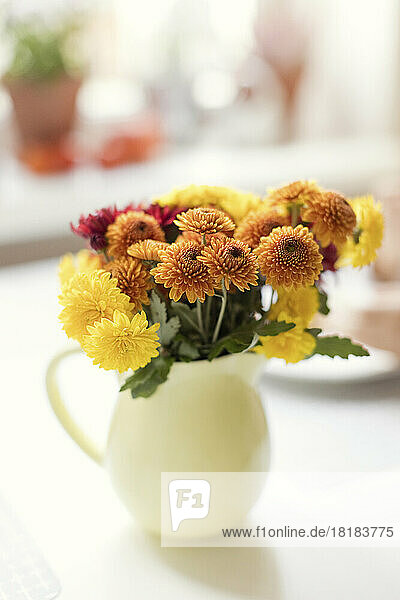 Yellow and orange chrysanthemum flowers in pitcher on table
