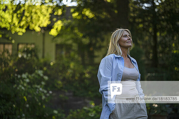 Contemplative mature woman standing with hands in pockets at garden