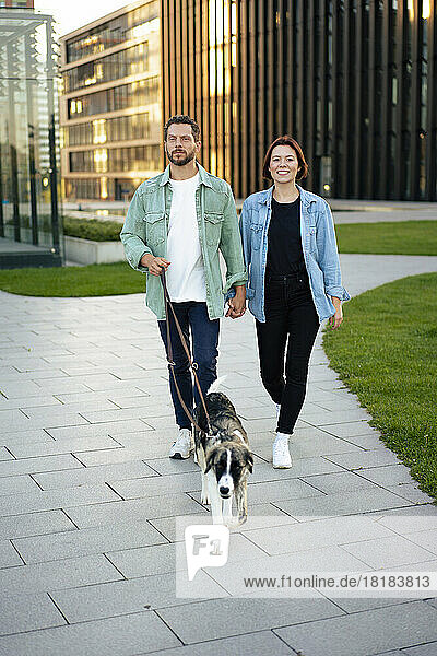 Man and woman strolling with dog on footpath