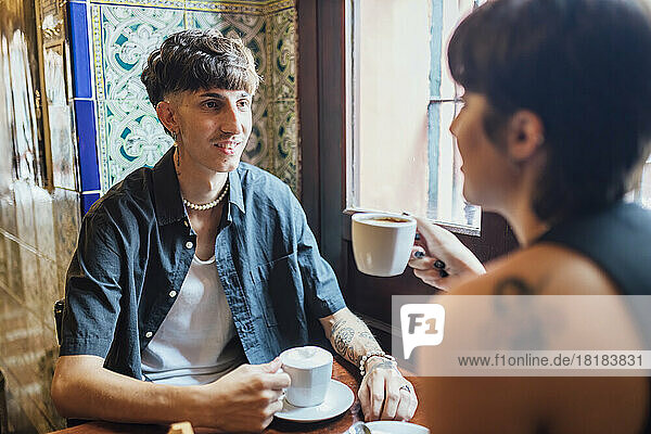 Hipster man looking at girlfriend holding coffee cup in cafe