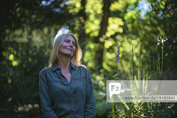 Thoughtful mature woman standing amidst plants in garden
