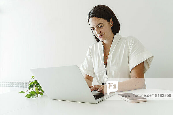 Lächelnde Geschäftsfrau  die zu Hause einen Laptop auf dem Tisch benutzt
