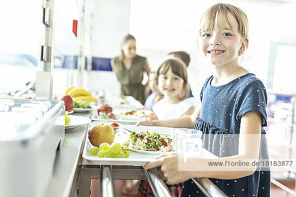 Blond smiling student with healthy meal at school cafeteria