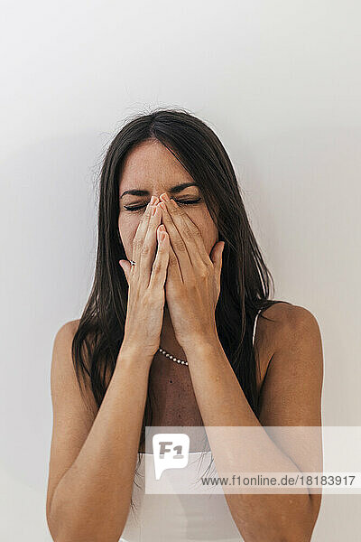 Sad woman covering mouth with hands standing in front of white wall