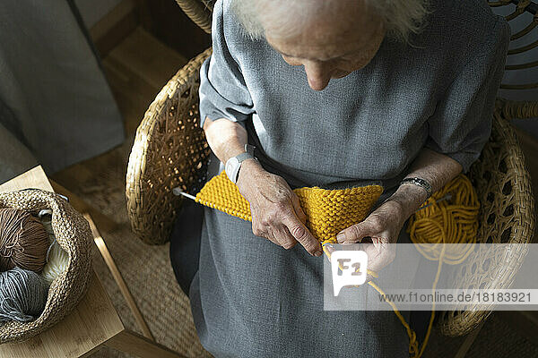 Senior woman knitting on chair at home